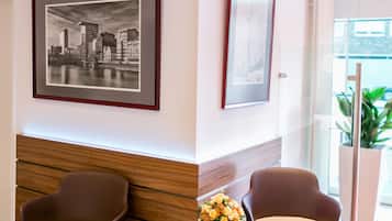 A reception area with two brown chairs, a small table with a magazine and a vase of flowers, and two framed pictures on the wall.