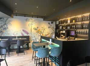 Zona de bar moderna con un mural, asientos y una barra con vasos y botellas.