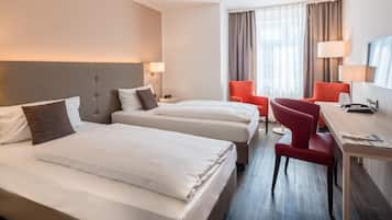 Ein Hotelzimmer mit zwei Betten, einem Schreibtisch, einem Stuhl, einem Fernseher und einem Fenster mit Vorhängen.