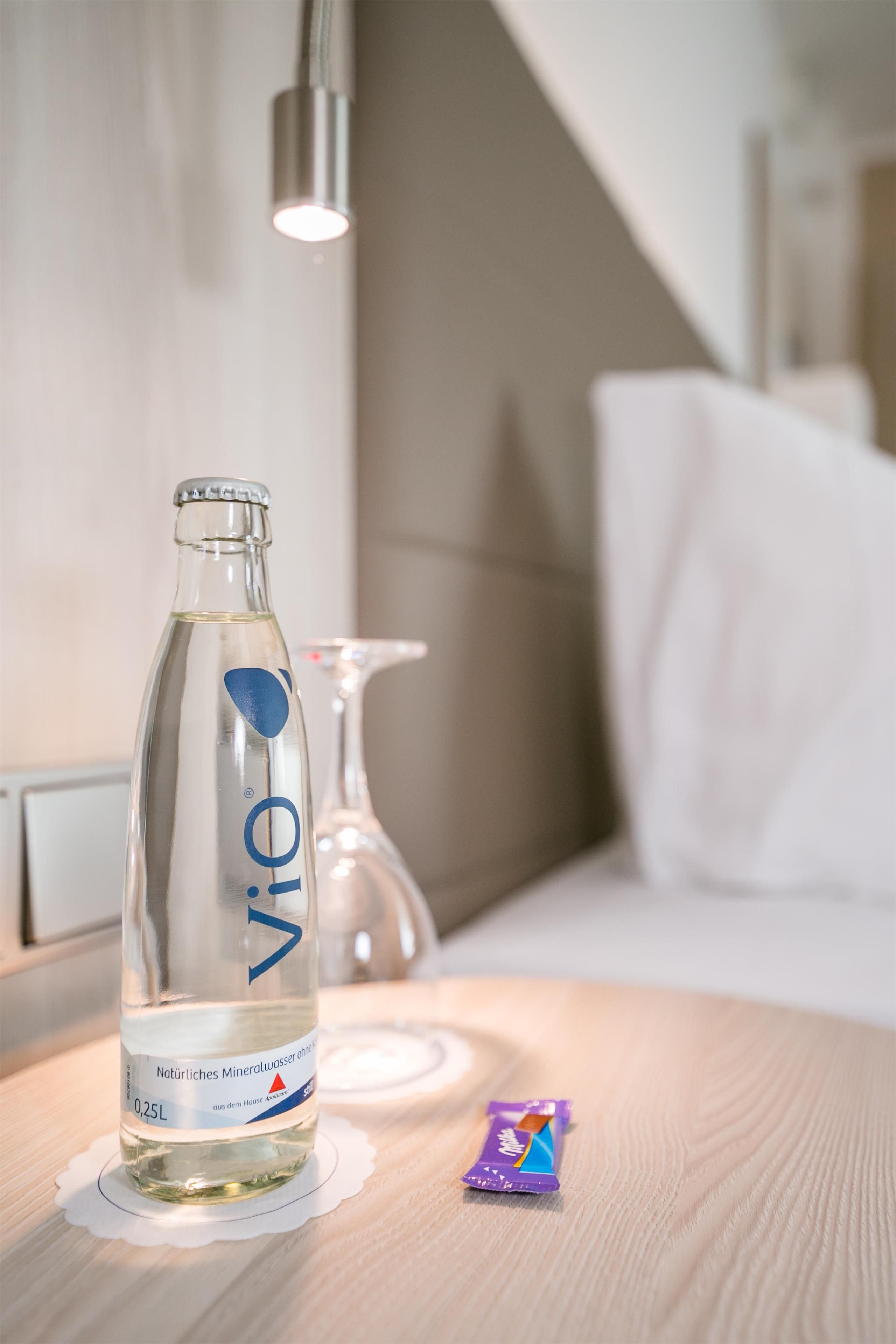A bottle of water on a table with a white pillow and a purple object beside it.
