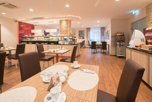 Ein Speisebereich eines Hotels mit mehreren Tischen, Stühlen und einer Buffettheke.