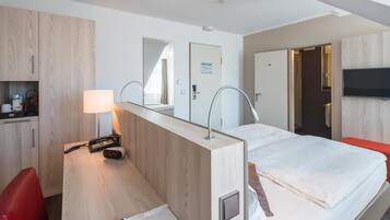 Ein Hotelzimmer mit einem Bett, einem Schreibtisch mit Lampe, einem Telefon und einem an der Wand befestigten Fernseher.