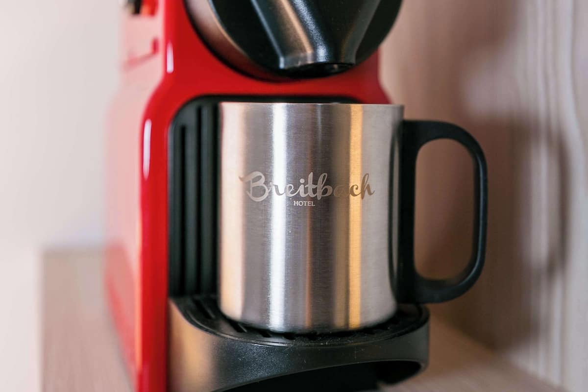 A red and silver coffee maker with a handle and a cup on a wooden surface.
