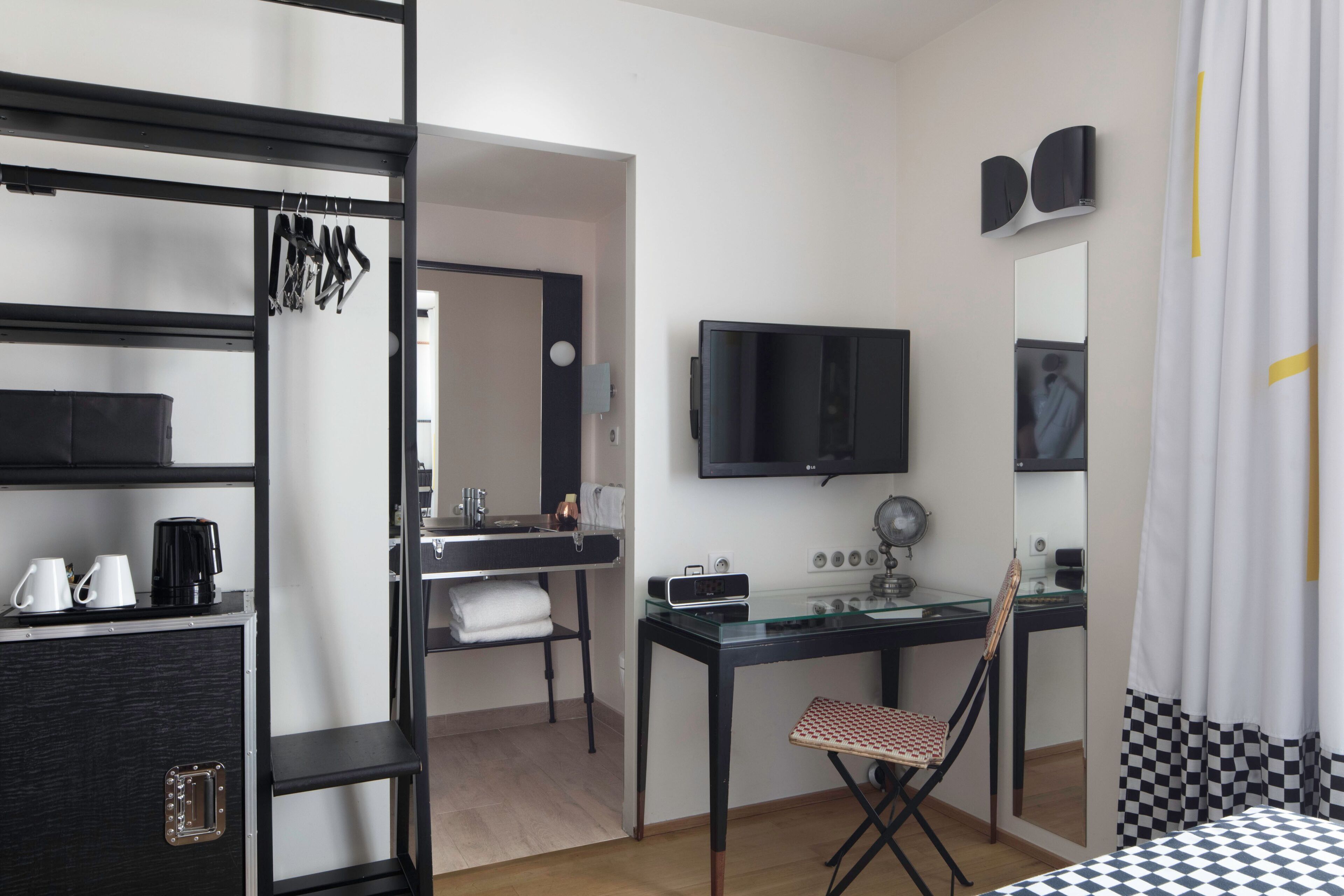 Una habitación de hotel moderna con cama, escritorio, silla, televisor, espejo y armario.
