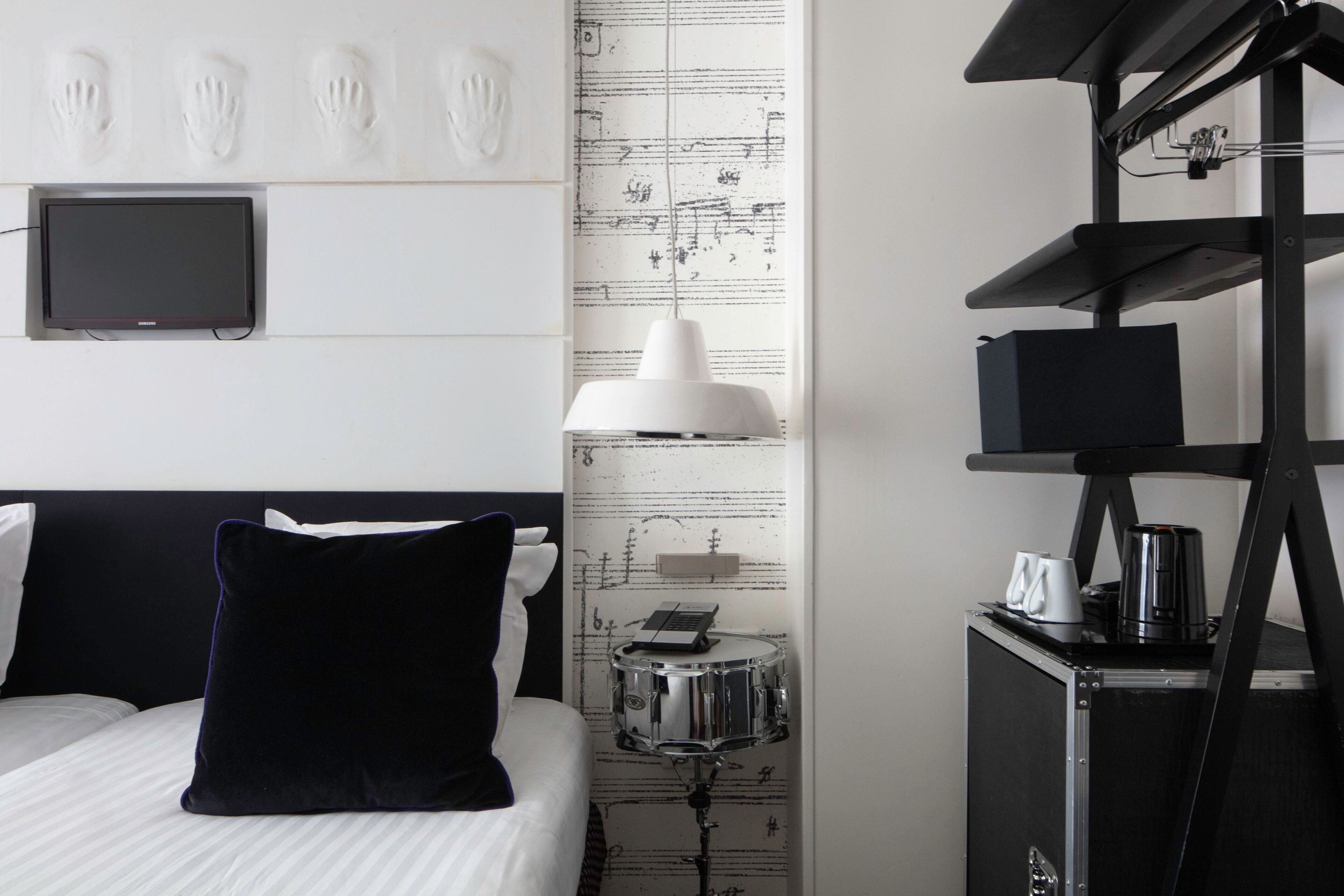 A hotel room with a bed, a desk with a lamp, a small table with a keyboard, and a shelf with a coffee maker.
