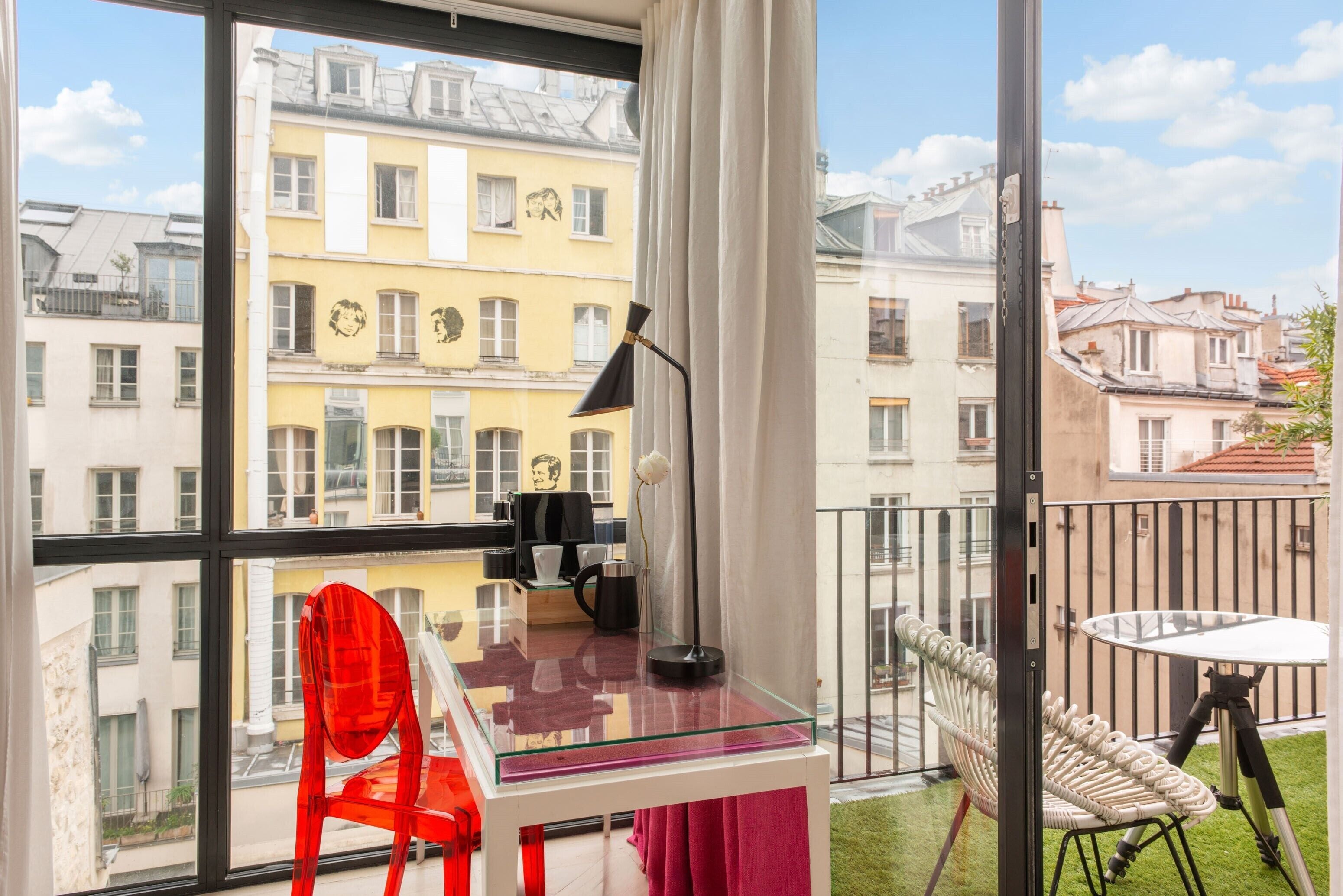 Un balcón con una mesa de vidrio, una silla roja y una silla blanca.