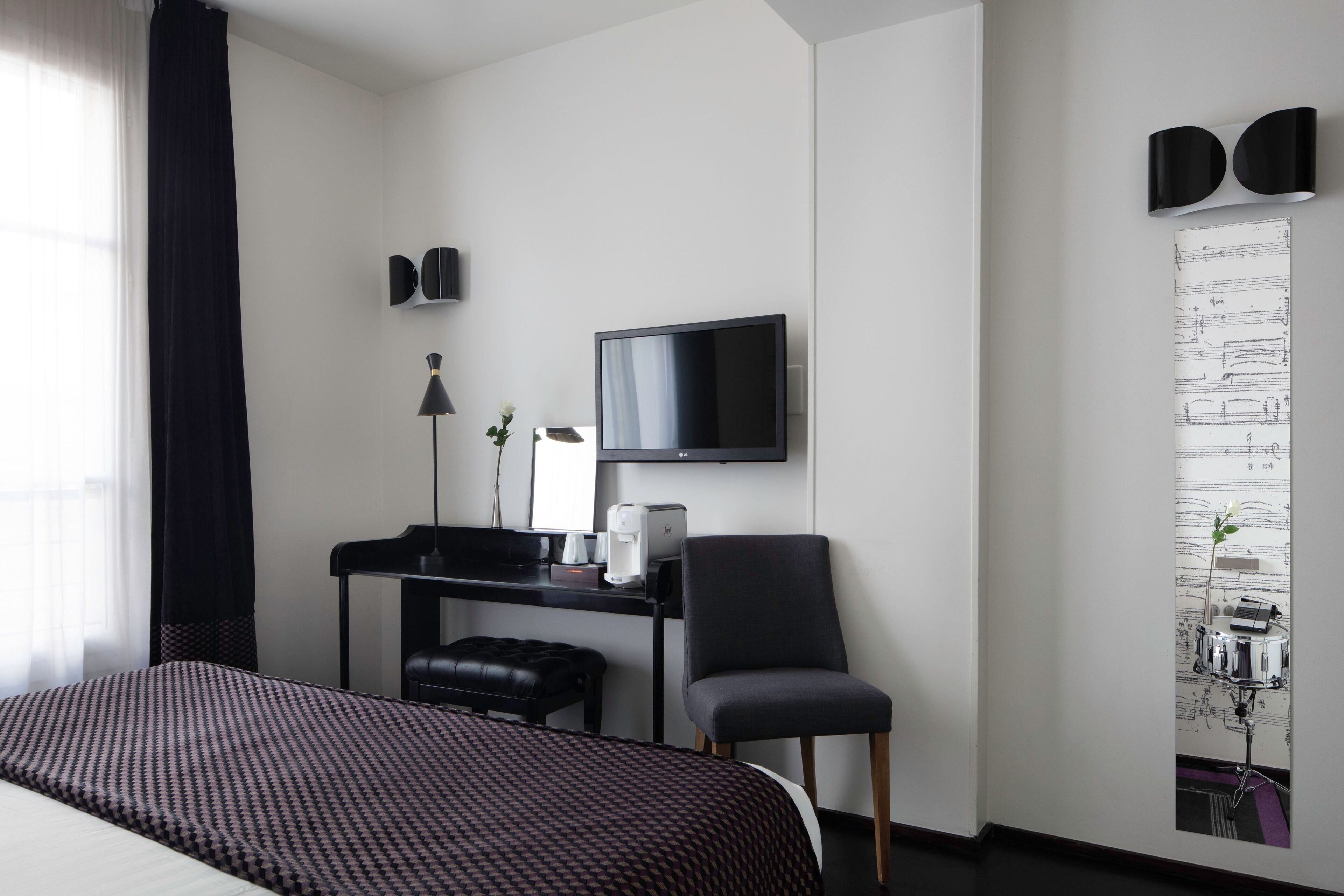 A hotel room with a bed, a desk with a chair, a television, and a wall-mounted artwork.