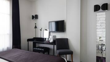 A hotel room with a bed, a desk with a chair, a television, and a wall-mounted artwork.