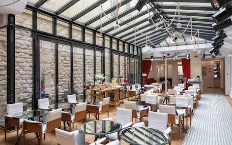 A spacious indoor area with a high ceiling, stone walls, and multiple seating arrangements including round tables and chairs.