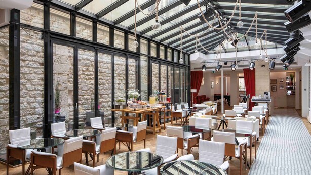 A spacious indoor area with a high ceiling, stone walls, and multiple seating arrangements including round tables and chairs.