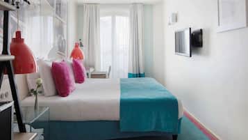 Habitación de hotel con cama, escritorio, silla, televisión y ventana con cortinas.