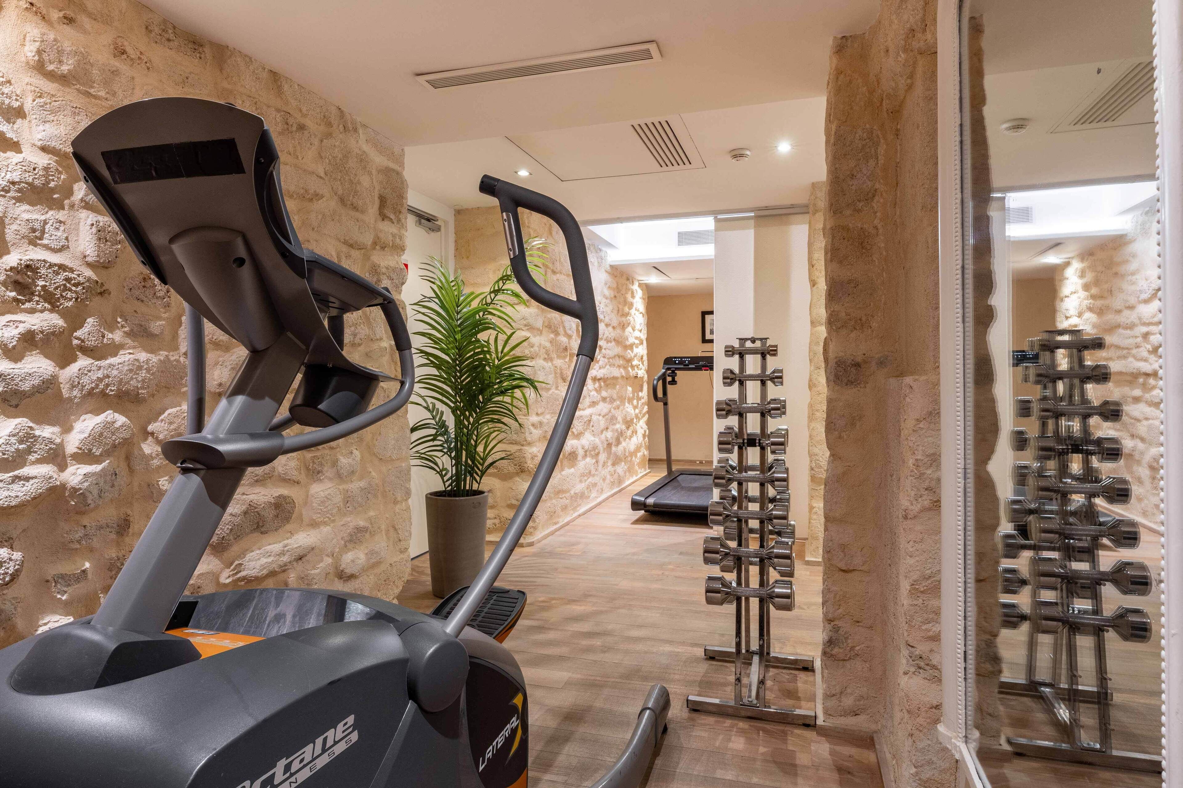 Zona de gimnasio con equipo de ejercicios, una cinta de correr y un estante de mancuernas fijado a la pared.