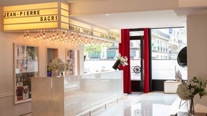 A hotel lobby with a reception desk, framed pictures on the walls, and a view of the street outside.