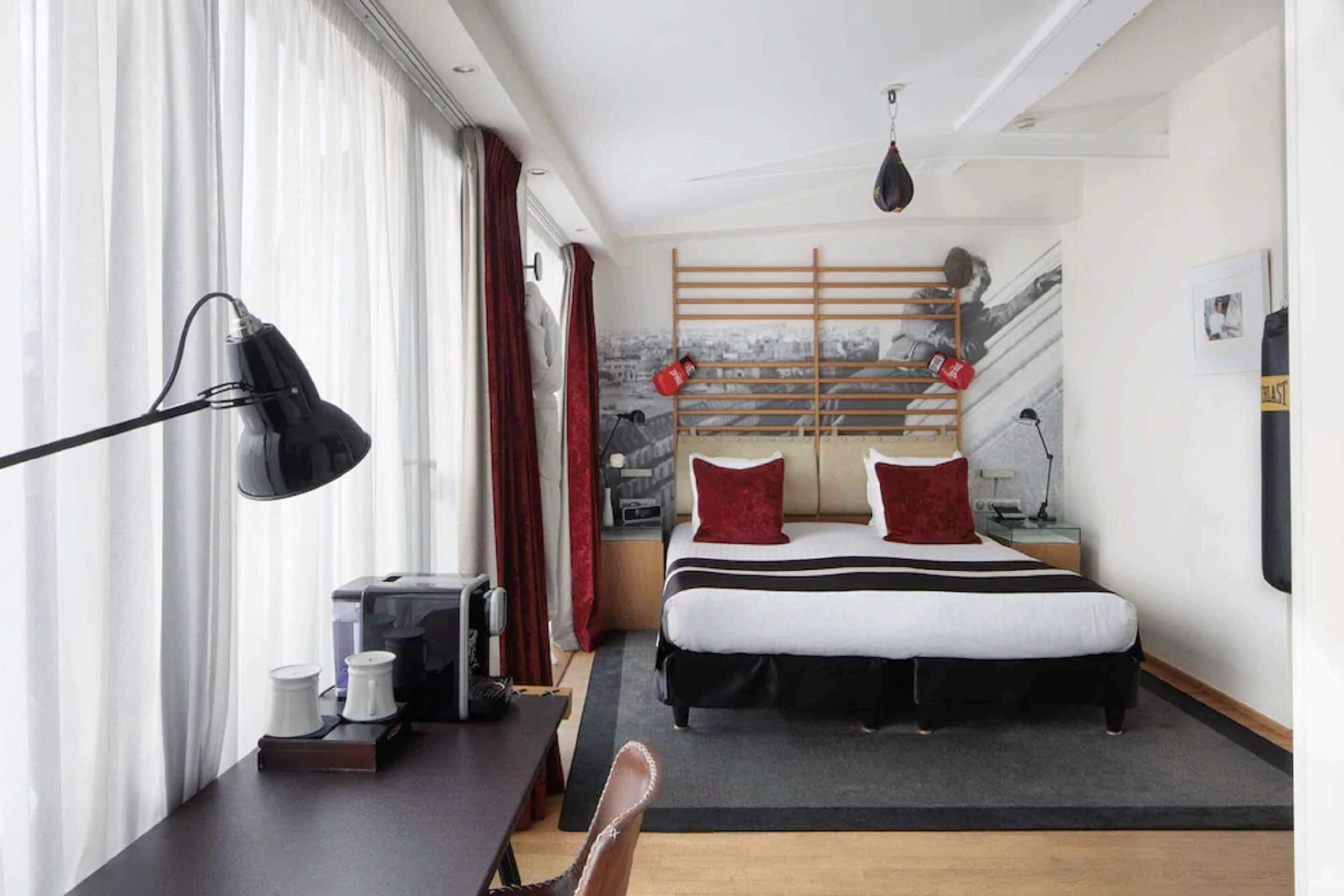 A hotel room with a bed, a desk with a lamp, a coffee maker, and a window with curtains.