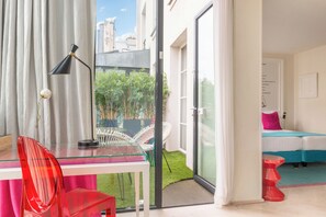 A modern room with a glass desk, a red chair, a bed with blue bedding, and a view of a garden through a sliding door. - Hôtel Le 123 Sébastopol - Astotel (Paris)