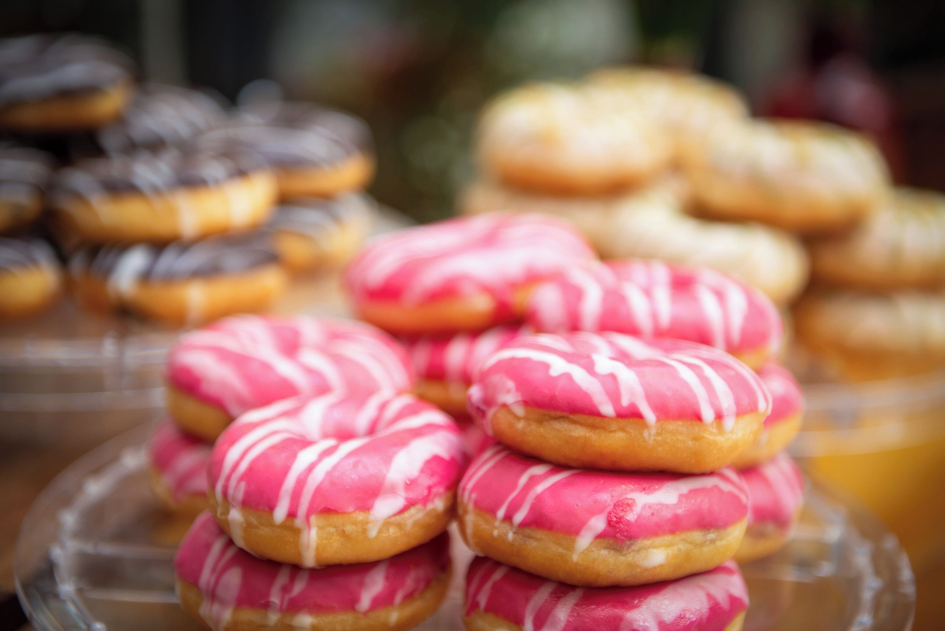 Une variété de beignets, dont certains sont recouverts d’un glaçage rose, sont présentés sur un plateau en verre.