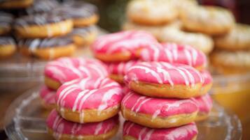 Une variété de beignets, dont certains sont recouverts d’un glaçage rose, sont présentés sur un plateau en verre.