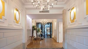 A hallway with a chandelier, white walls with gold accents, and a door leading to a dining area.