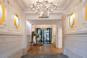 A hallway with a chandelier, white walls with gold accents, and a door leading to a dining area.