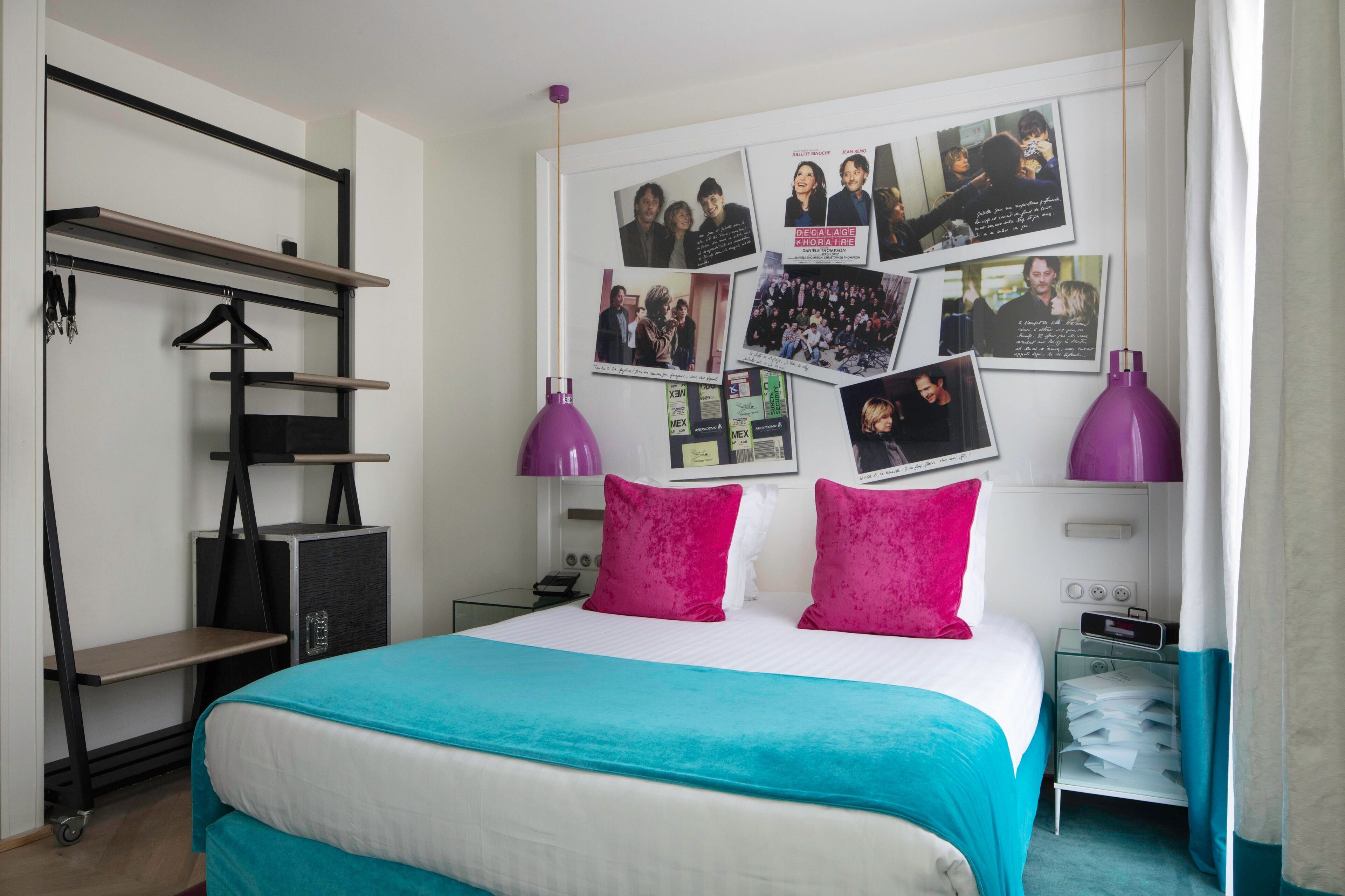 A bedroom with a bed, a wardrobe, a desk, and a wall decorated with photos.