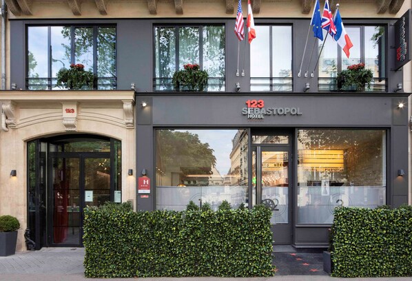 The exterior of the 123 Sebastopol Hotel with a modern facade, large windows, and flags. - Hôtel Le 123 Sébastopol - Astotel (Paris)