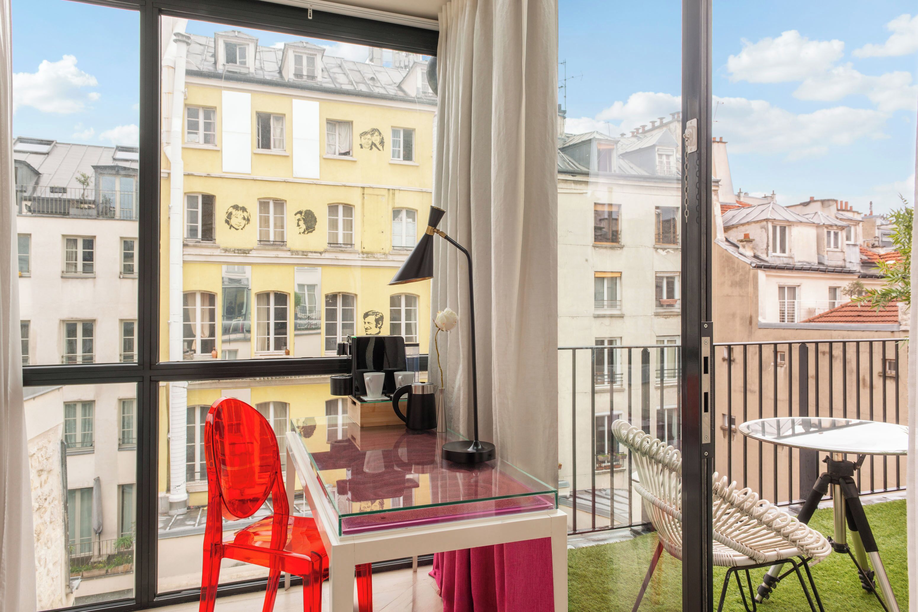A balcony with a glass table, a red chair, and a white chair.