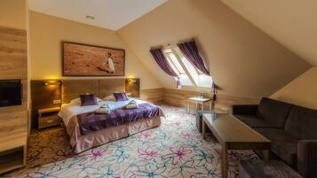 Een slaapkamer met een bed, een bank, een klein tafeltje en een raam met gordijnen.