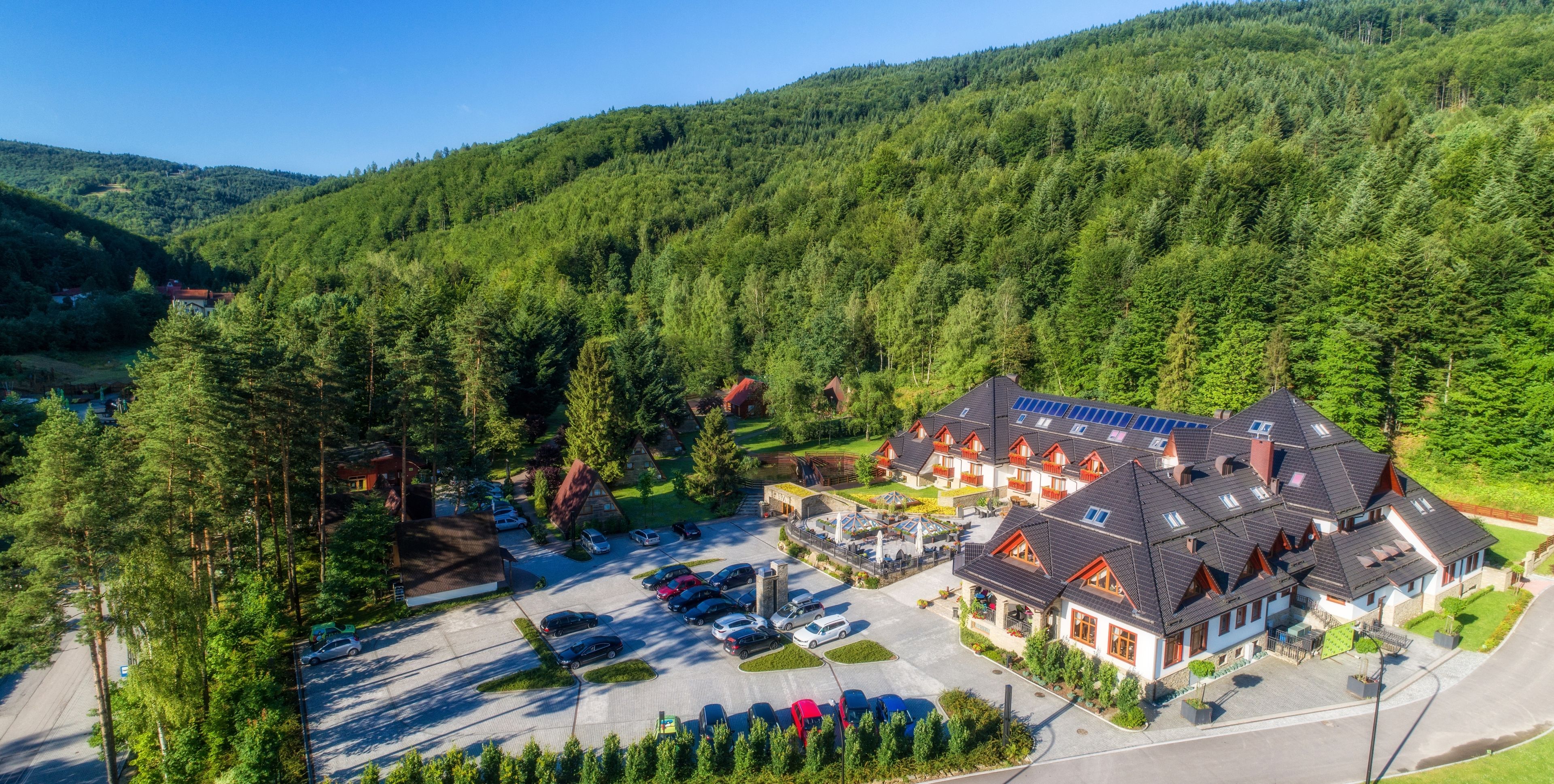 A large, multi-story hotel with a parking lot and a scenic forested hillside in the background.