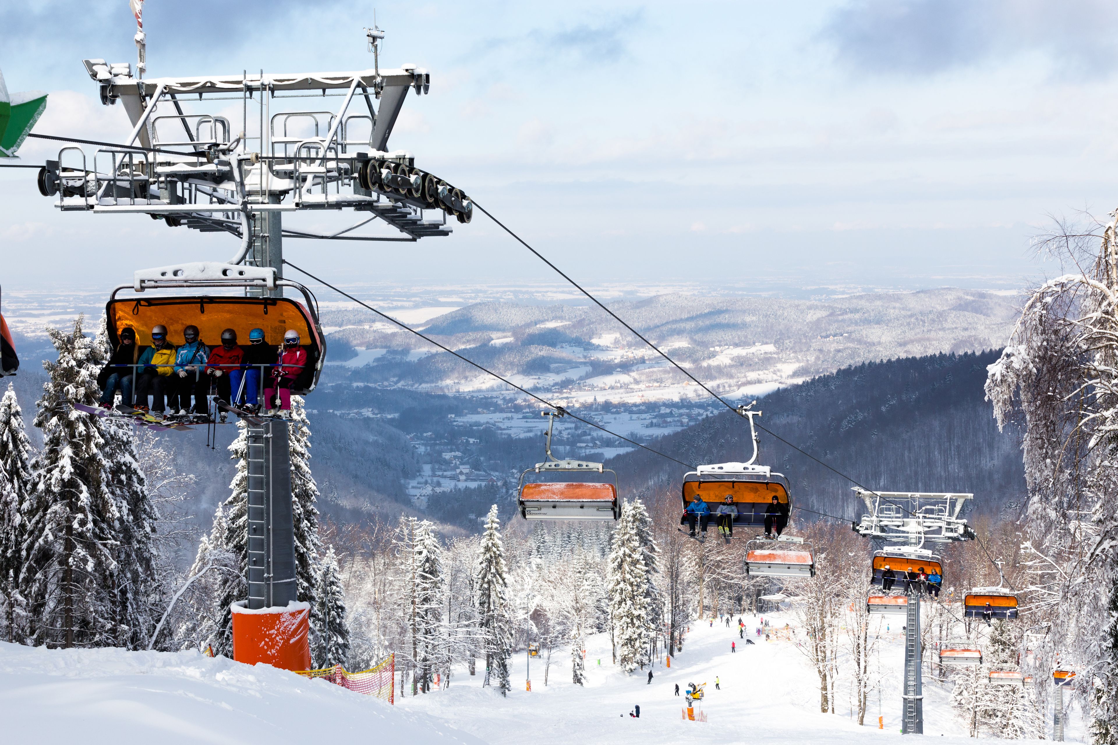A ski lift with passengers, surrounded by snow-covered trees and mountains in the background.