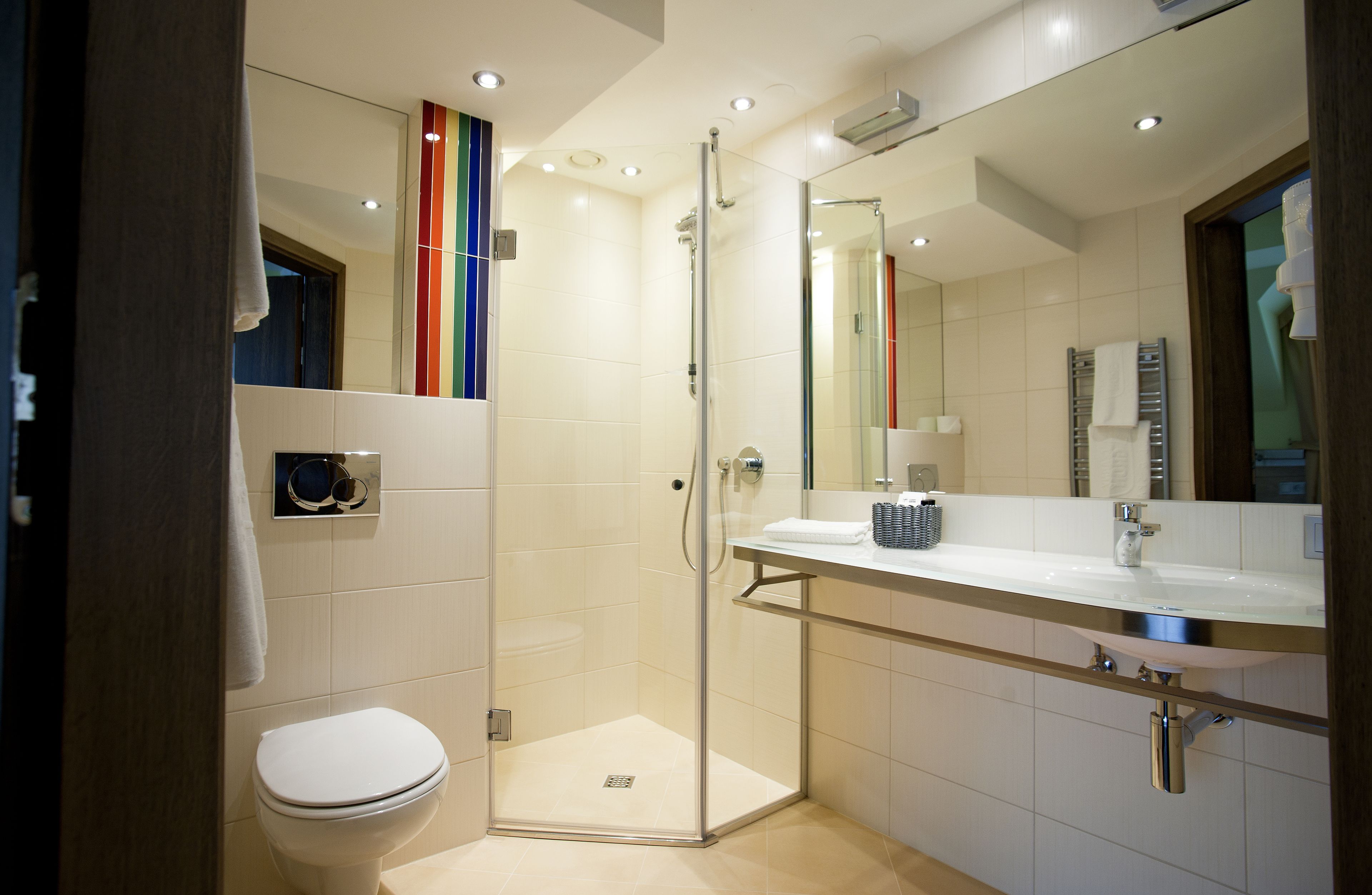 A modern bathroom with a glass shower enclosure, a white toilet, and a large mirror above the sink.