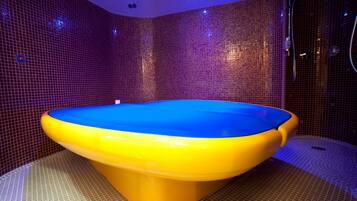 A large, uniquely shaped bathtub with a blue top and yellow sides, set against a tiled wall in a bathroom.