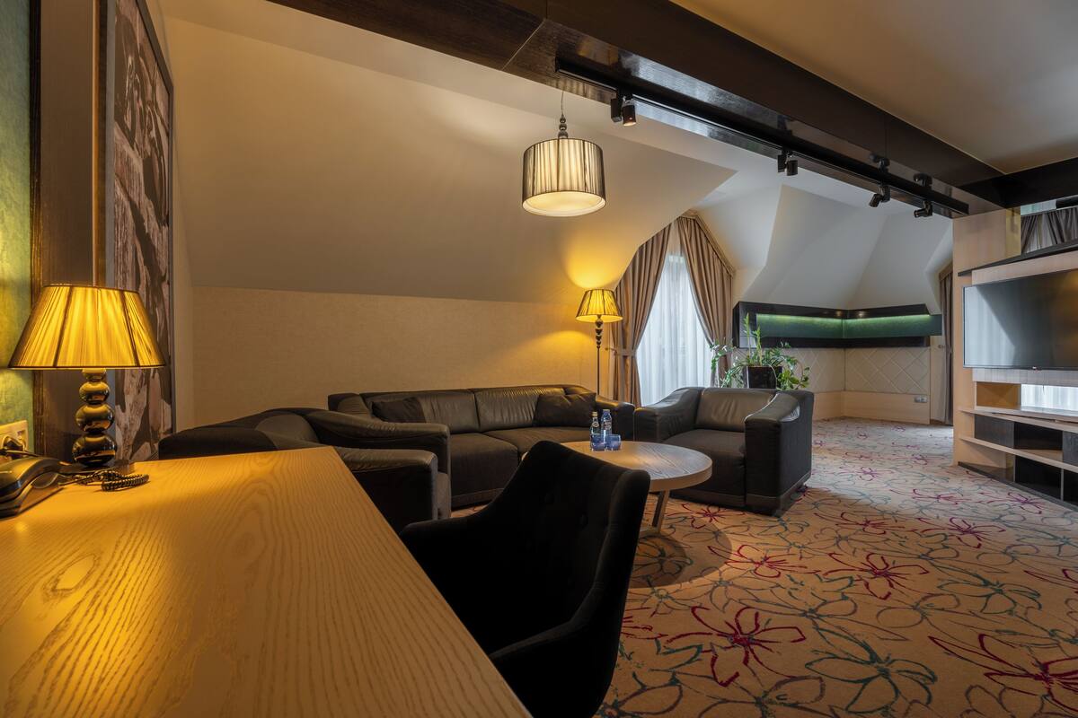 A hotel room with a wooden table, two sofas, a small round table, and a TV on a stand.