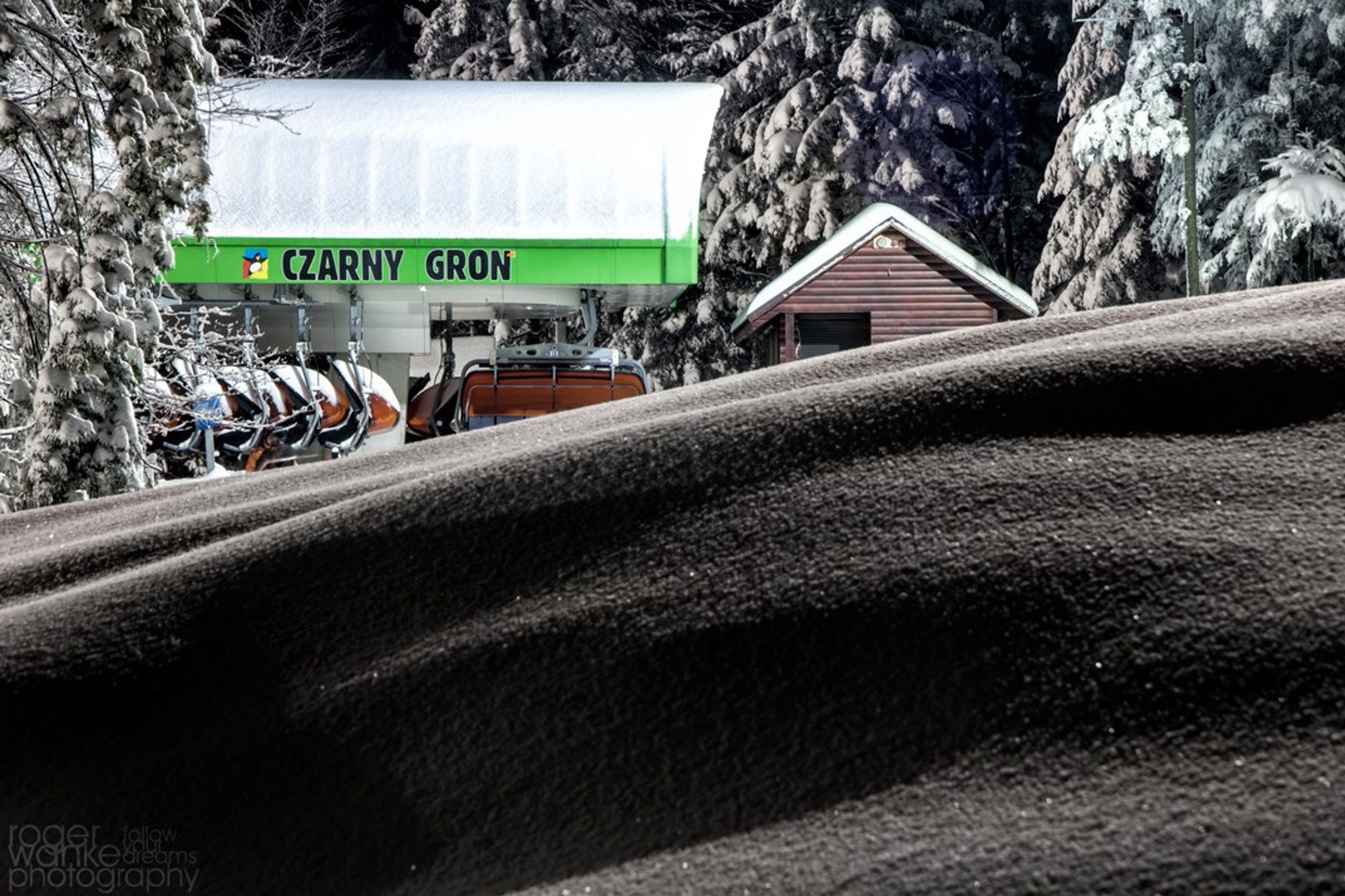 A gas station named CZARNY GRON with a row of parked vehicles and a building with a sloped roof.