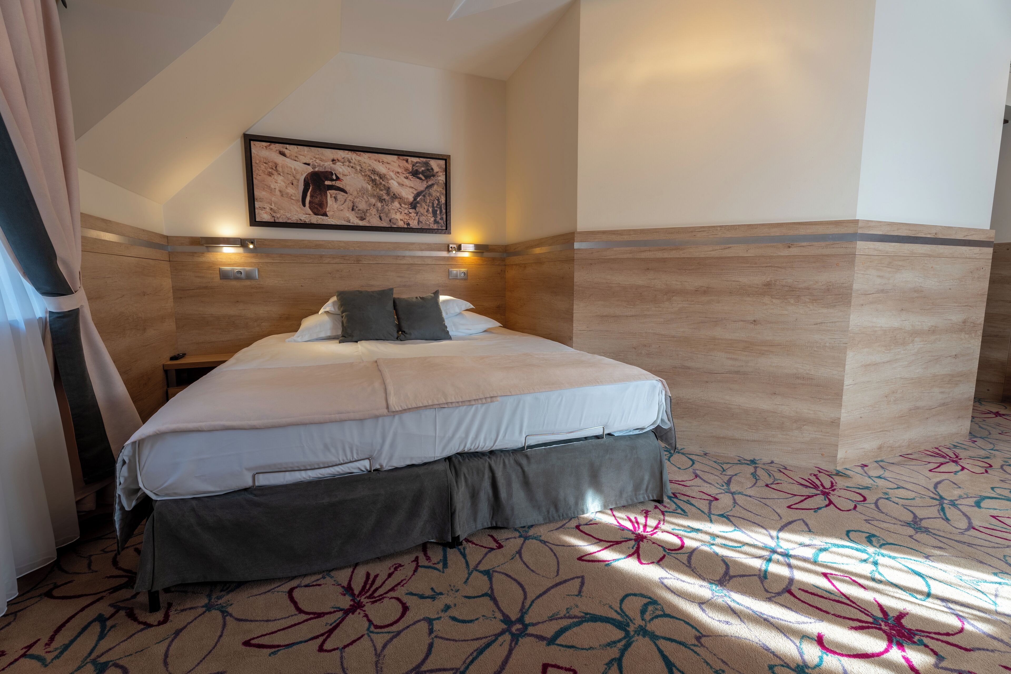 A hotel room with a bed, a nightstand, a wall-mounted light, and a framed picture on the wall.
