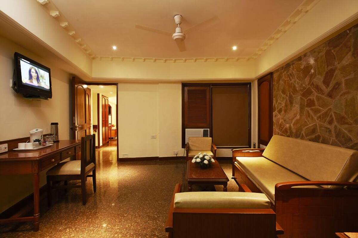 Quarto de hotel com escrivaninha de madeira, sofá, televisão e parede de pedra.