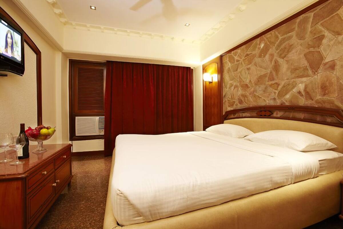 Quarto de hotel com uma cama, penteadeira de madeira, televisão e parede de pedra.