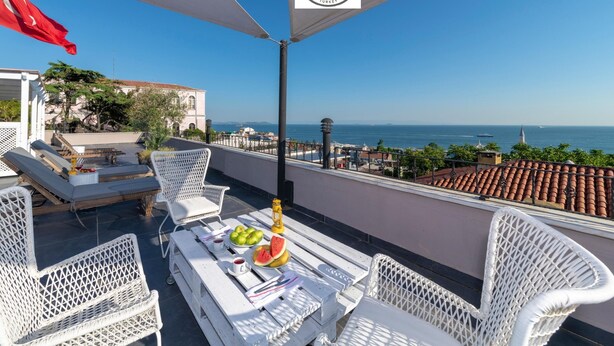 A terrace with white wicker furniture, a table with fruits and a candle, and a view of the sea. - Rumours Inn (Istanbul)