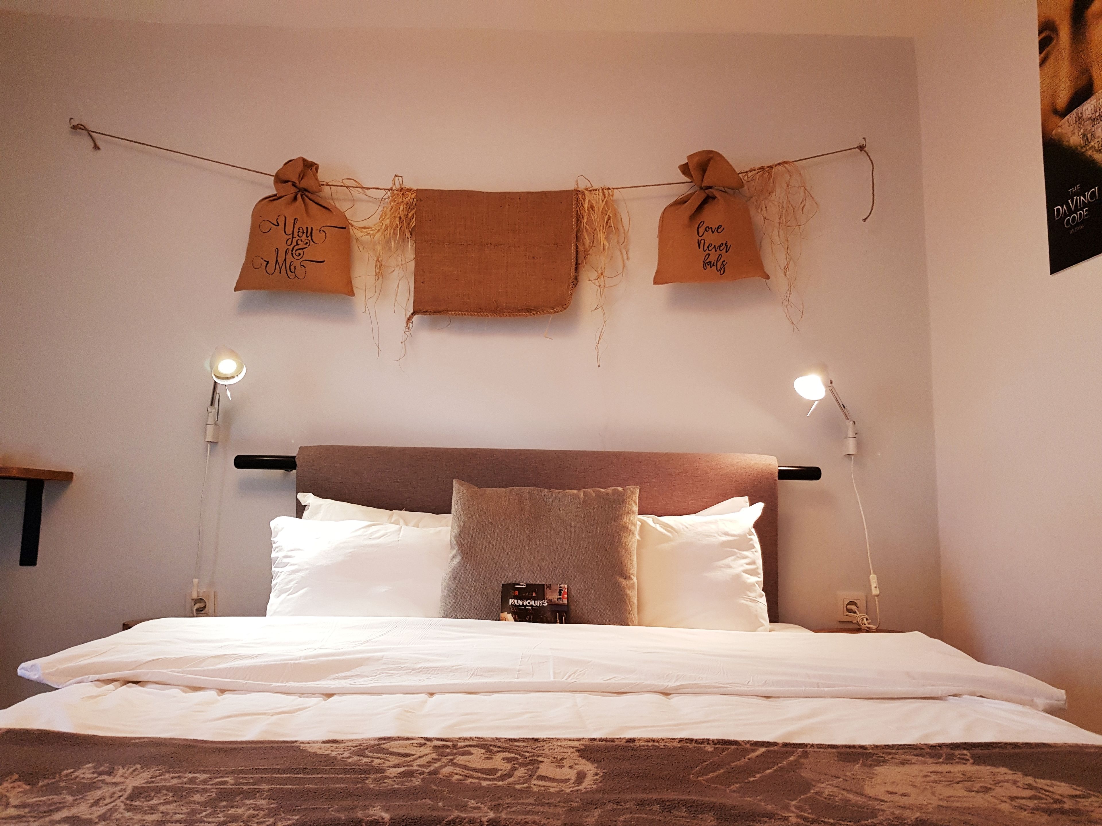 A neatly made bed with white linens, a brown headboard, and two bedside lamps.