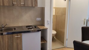A compact kitchen with a sink, stove, and countertop, adjacent to a toilet and a small dining area. - The Hostel (Hamburg)