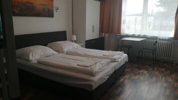 Una cama doble con cabecera, un escritorio con silla, un radiador y una ventana con cortinas.