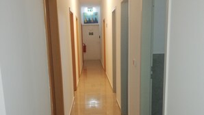 A hallway with doors on both sides, a fire extinguisher on the left wall, and a sign above the door at the end. - The Hostel (Hamburg)