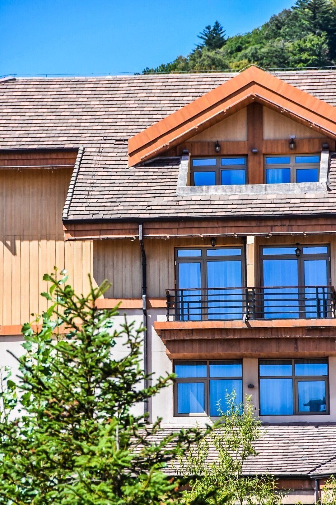 A multi-story building with a sloped roof, large windows, and a balcony on the upper floor.