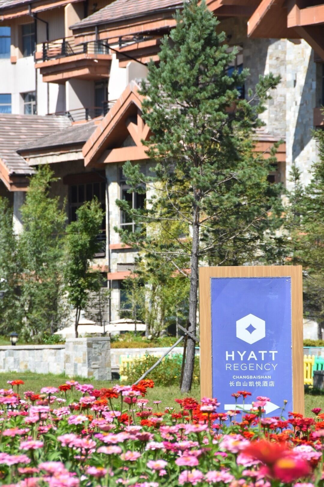 A sign for a Hyatt Regency hotel with a mountain backdrop and a garden with colorful flowers.