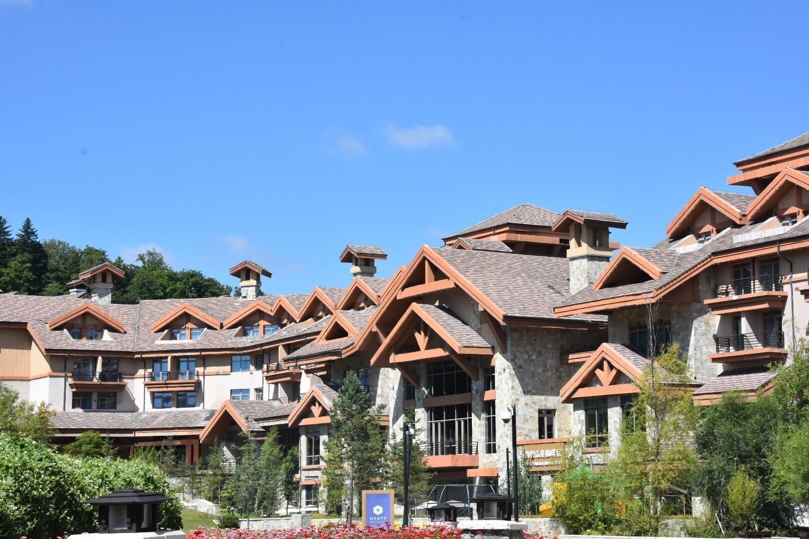 A hotel with multiple buildings featuring stone facades and wooden accents, a clear blue sky, and a sign indicating it is a Hyatt hotel.