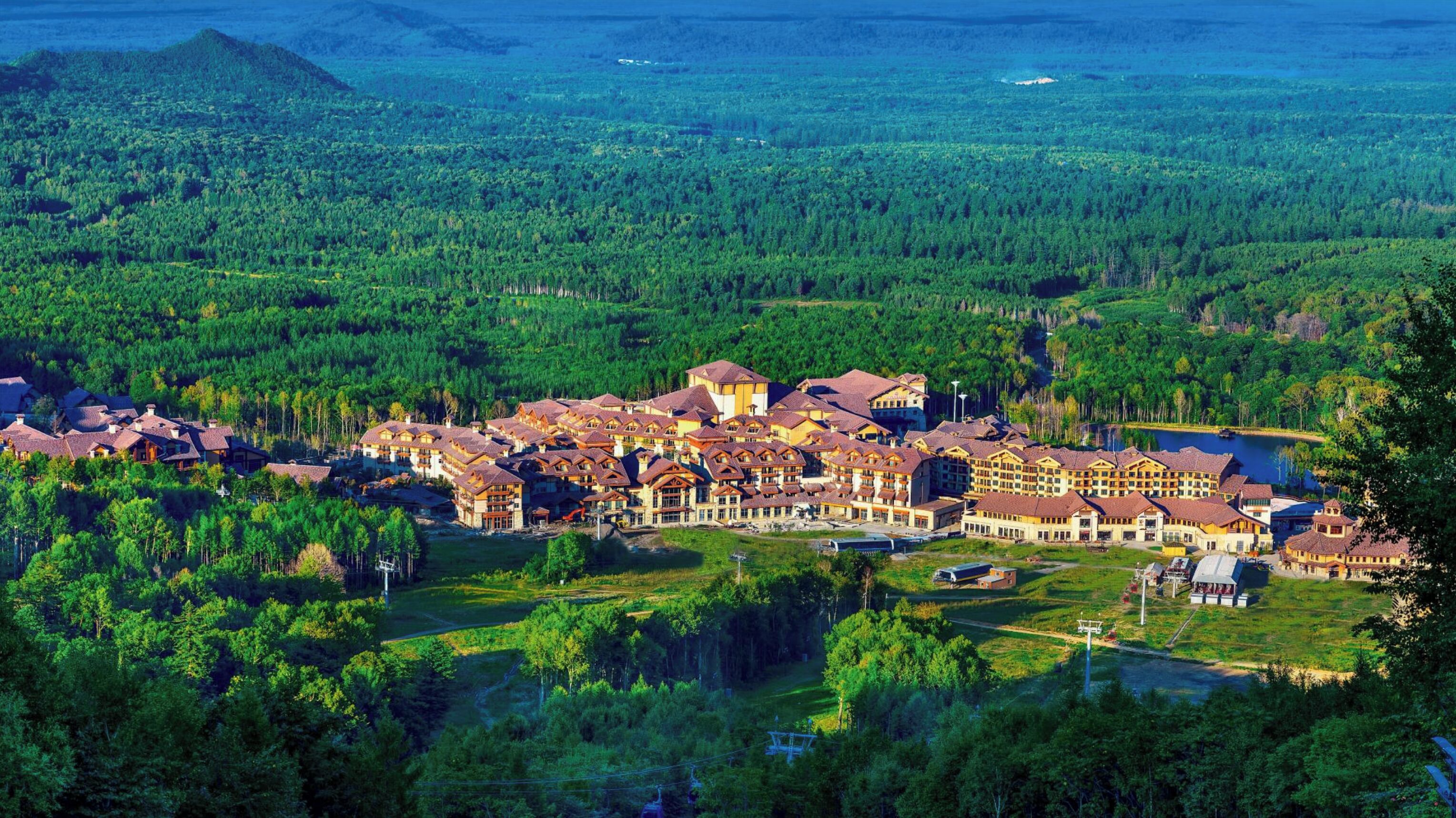 A large resort with multiple buildings, surrounded by dense forest and a lake.