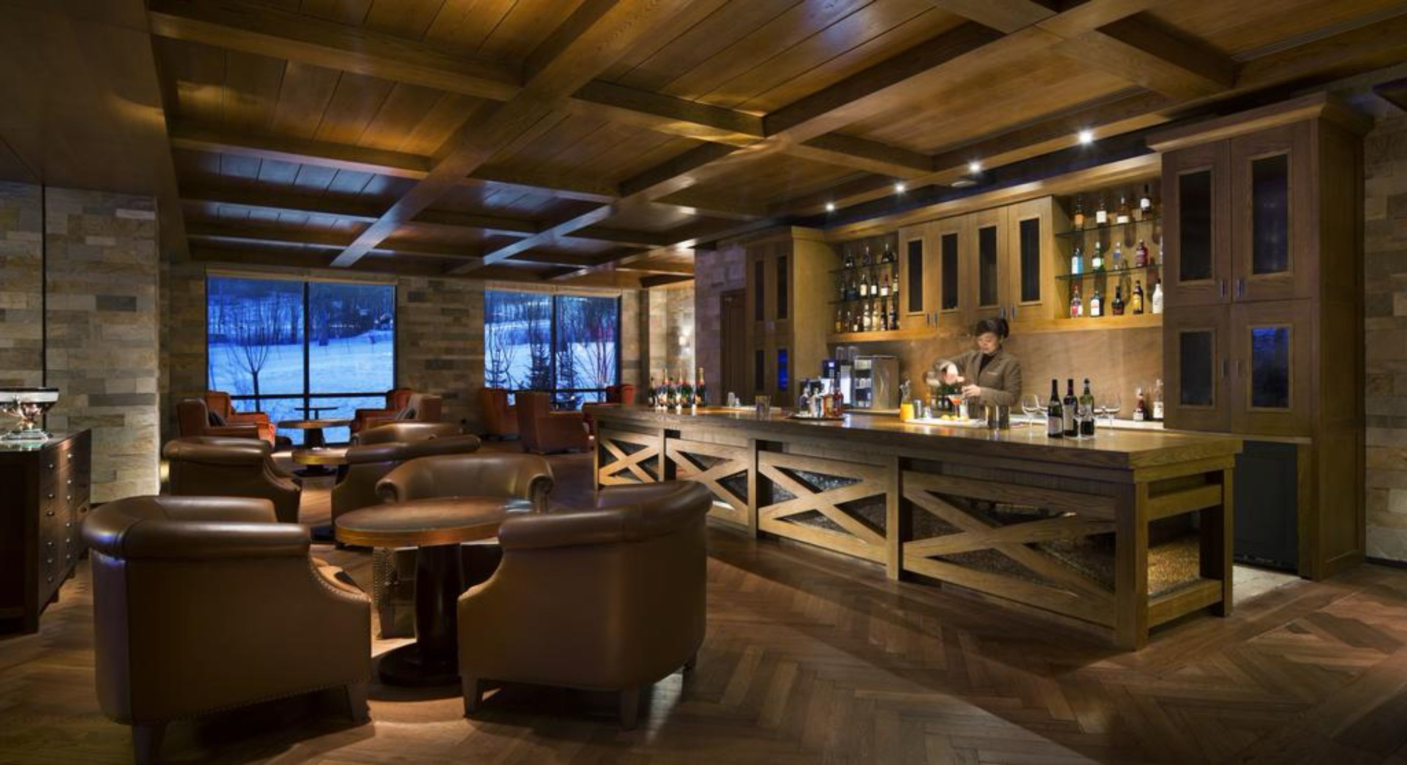 A bar area with wooden furniture, a bar counter, and a view of a snowy landscape through large windows.
