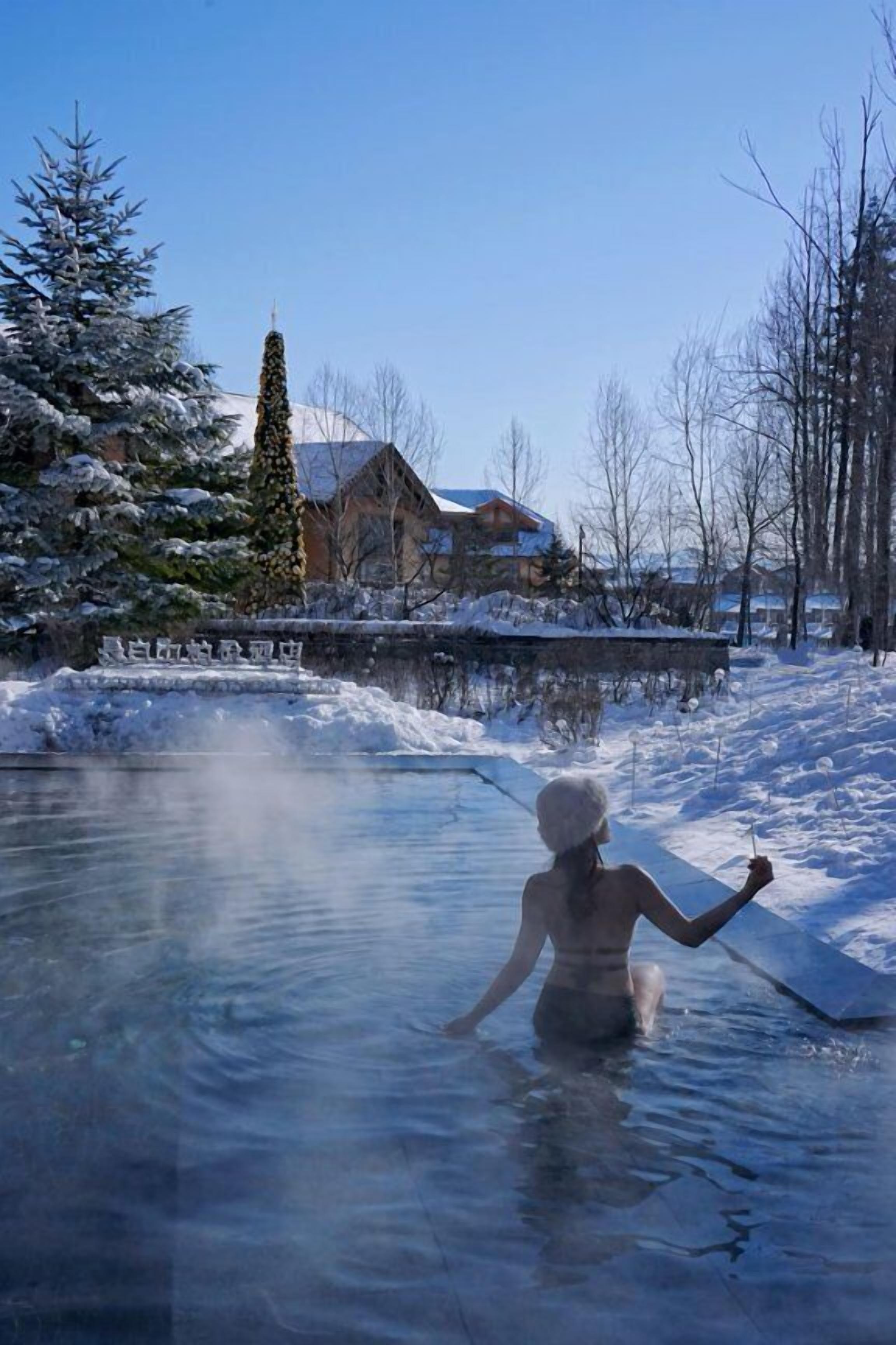 A person in a natural setting with a body of water, trees, and a building in the background.