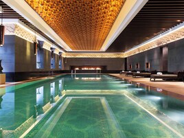 Una amplia piscina interior con piso de diseño geométrico, una chimenea decorativa y áreas de descanso con asientos.
