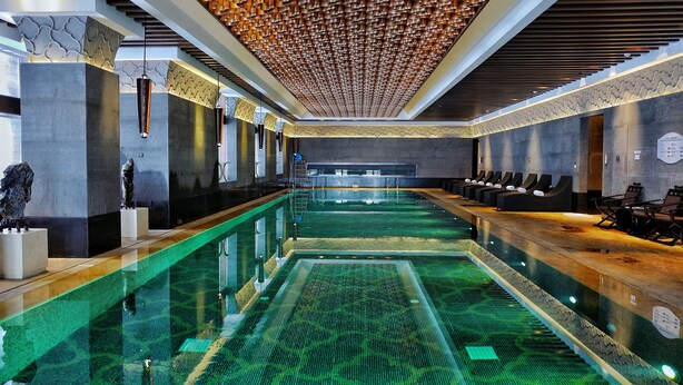 Una piscina interior moderna con un diseño largo y estrecho, rodeada de zonas de estar y un techo con diseños.