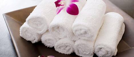 A set of neatly rolled white towels on a square tray with a purple orchid.